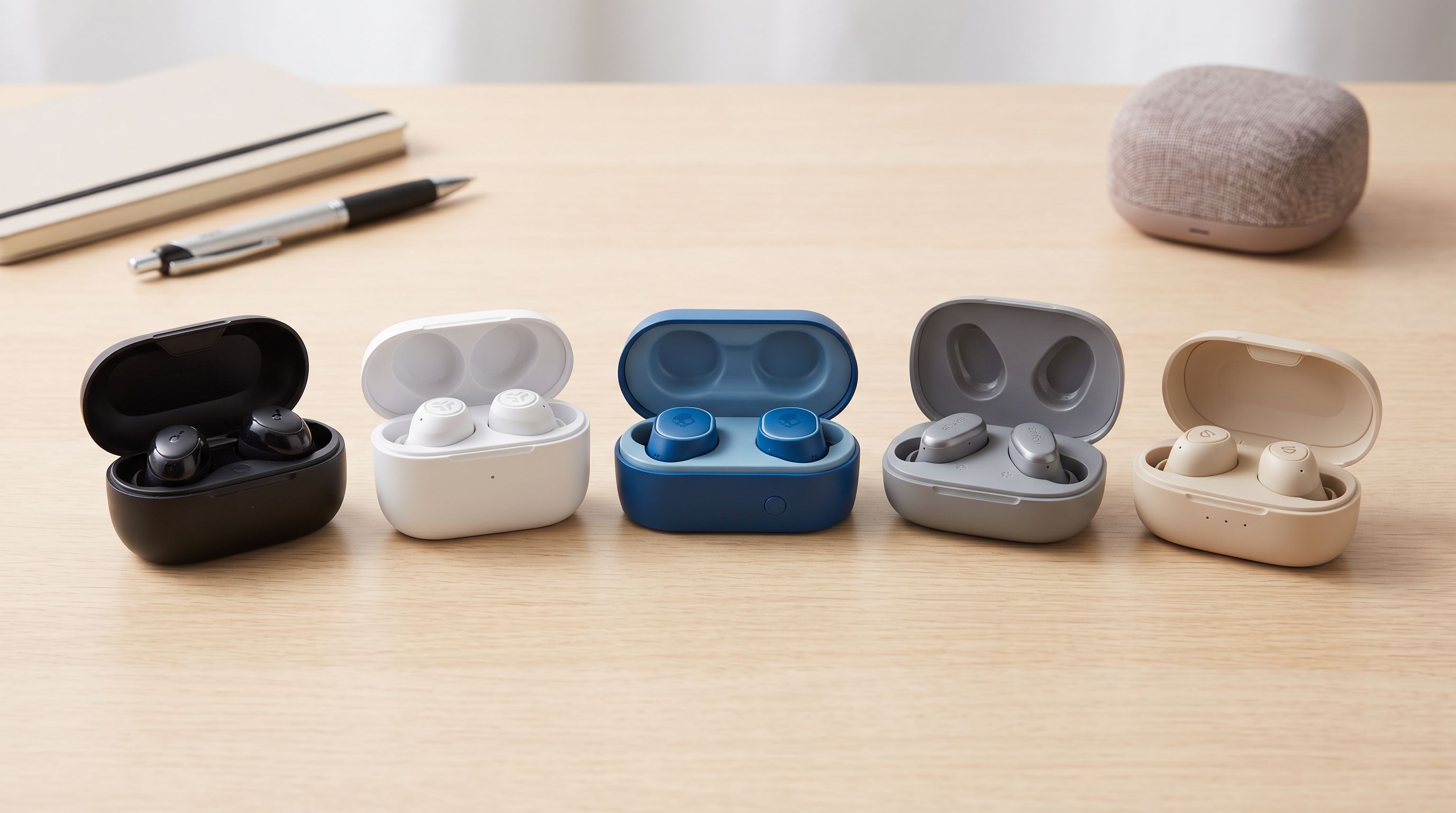 Five pairs of budget active noise cancelling wireless earbuds in their charging cases arranged on a desk