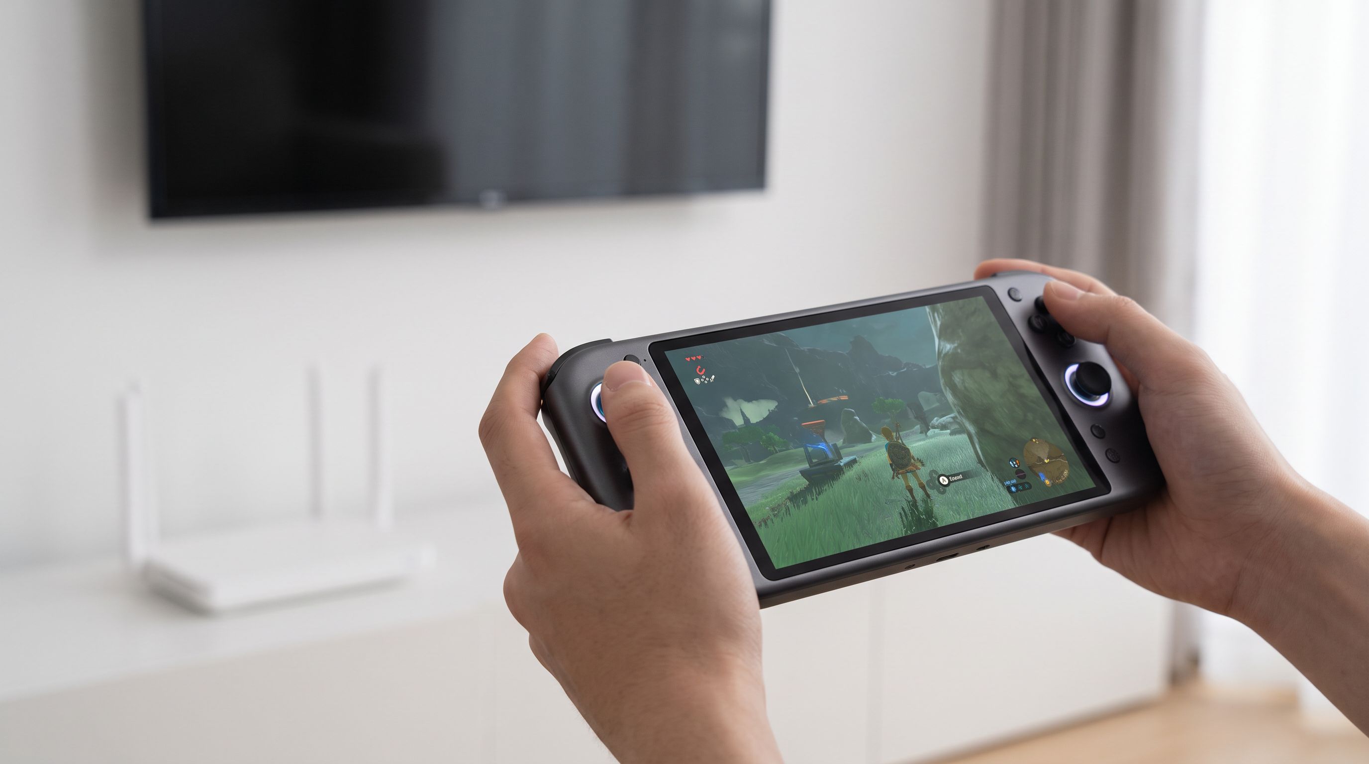 A handheld gaming device held in two hands streaming a game over Wi-Fi, with a router and TV blurred in the background