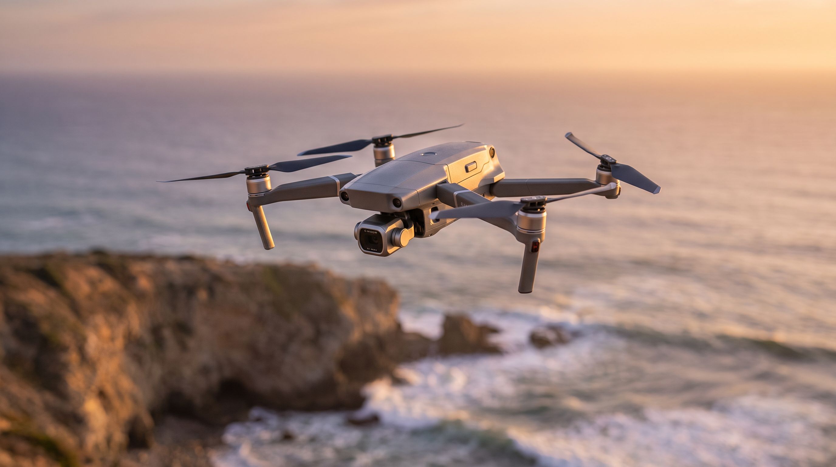 A folding camera drone hovering above a coastal cliff at golden hour, gimbal camera angled toward the horizon