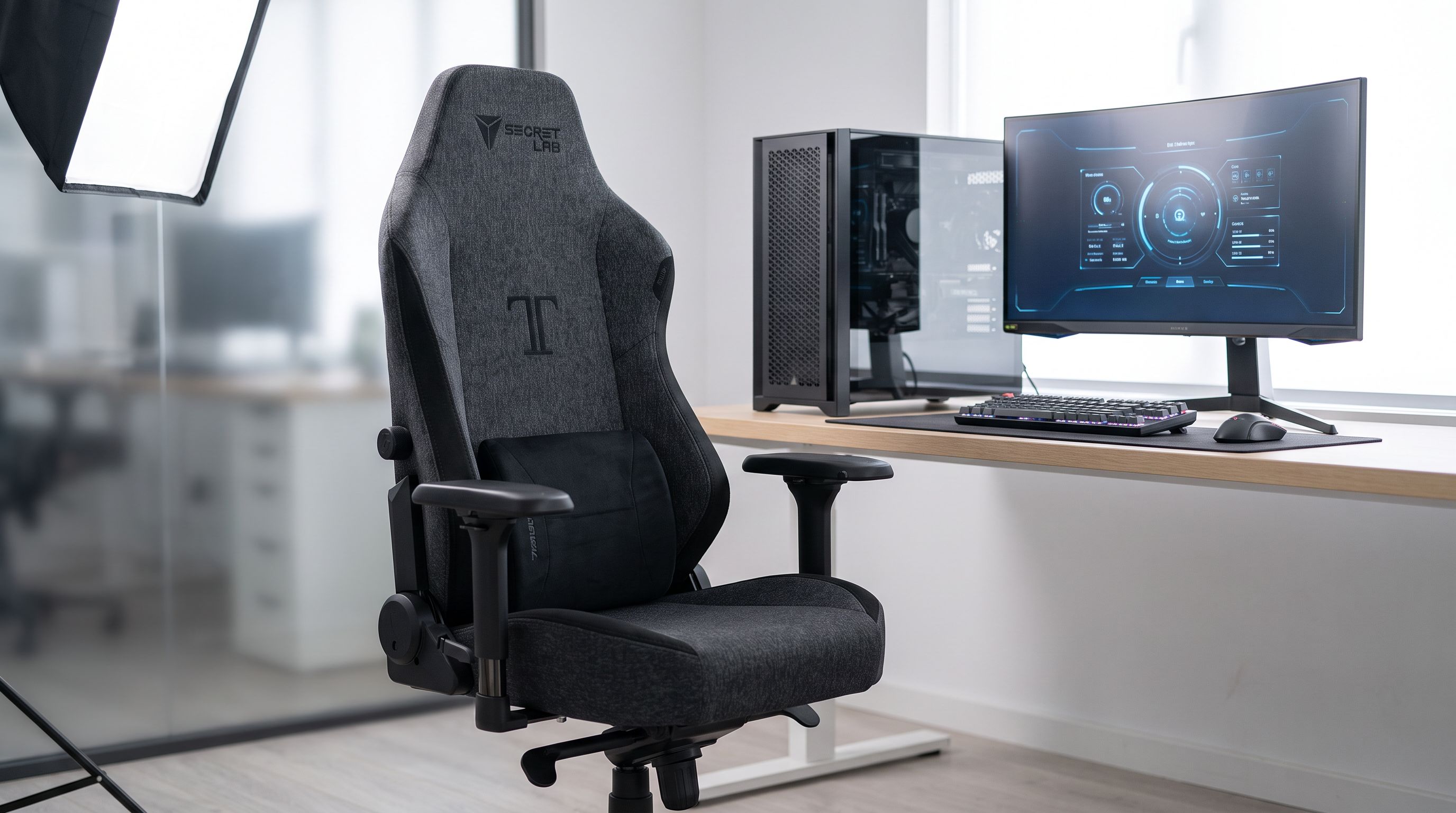 A black and grey fabric gaming chair with 4D armrests and lumbar support positioned at a desk with a PC and ultrawide monitor
