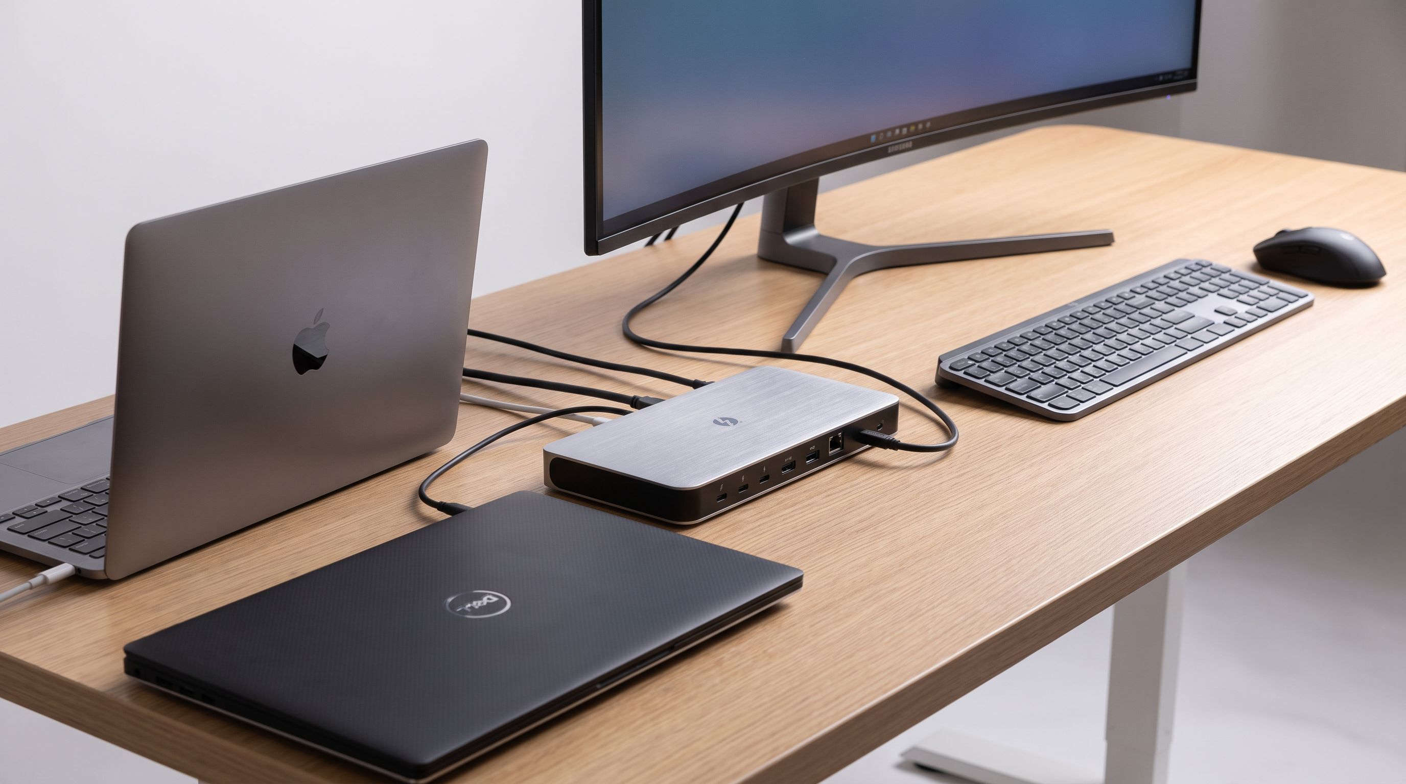 A Thunderbolt docking station on a desk connected to a monitor, keyboard and mouse with two laptops beside it
