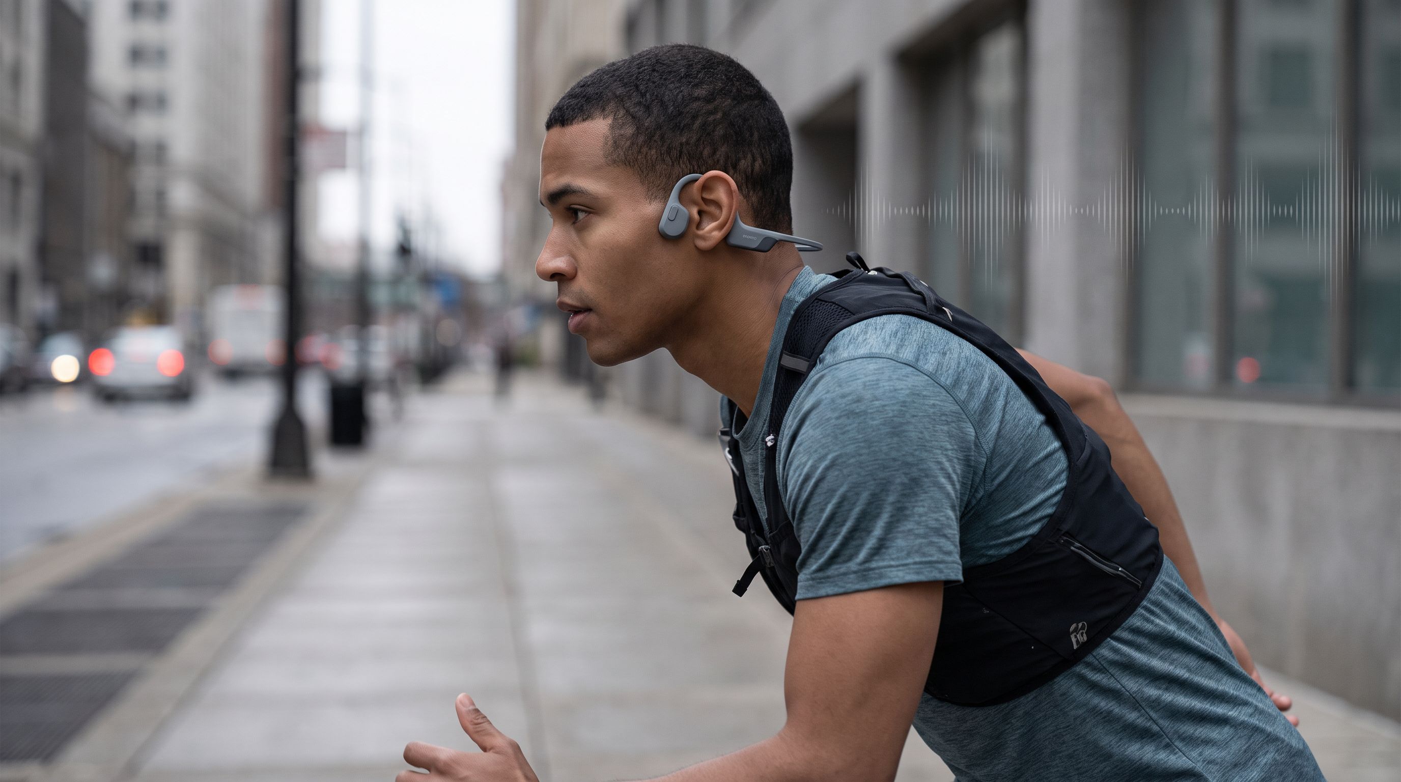 A runner on a city street wearing open-ear bone conduction headphones that leave the ear canal uncovered