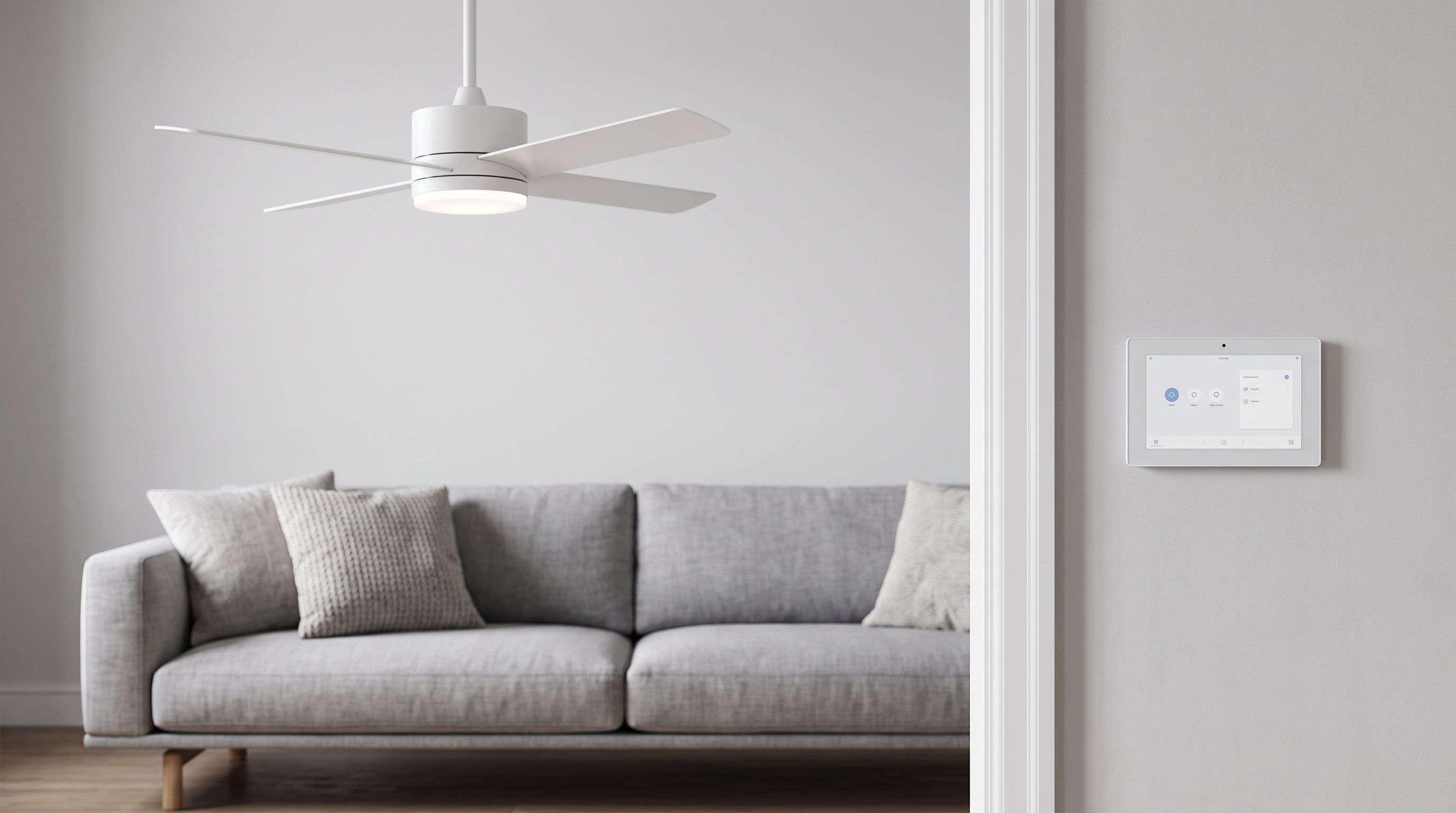 A white ceiling fan with light kit above a living room sofa, with a smart wall control panel mounted beside the doorway